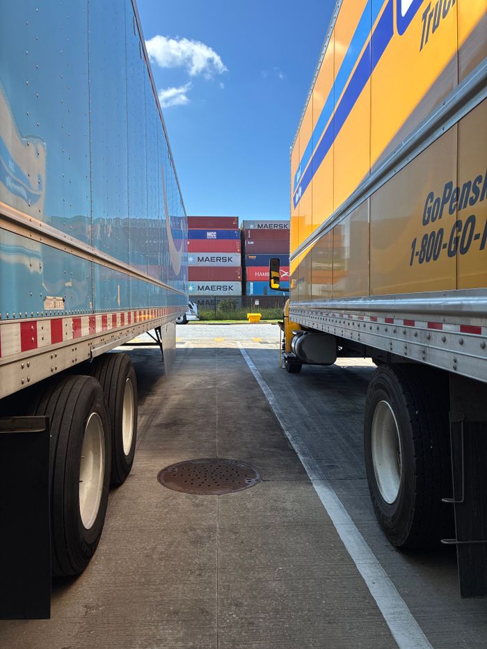 About Wide shot of parked trailers with shipping containers in the background, clear sunny day.