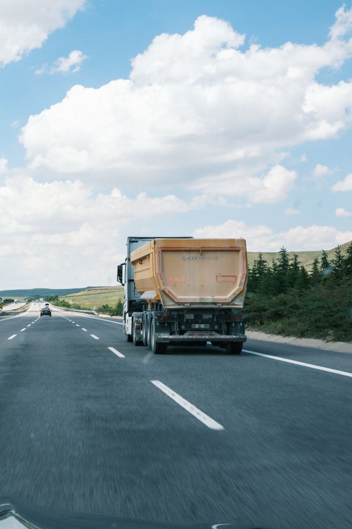 Services A cargo truck travels on a highway beneath a bright blue sky with fluffy clouds.