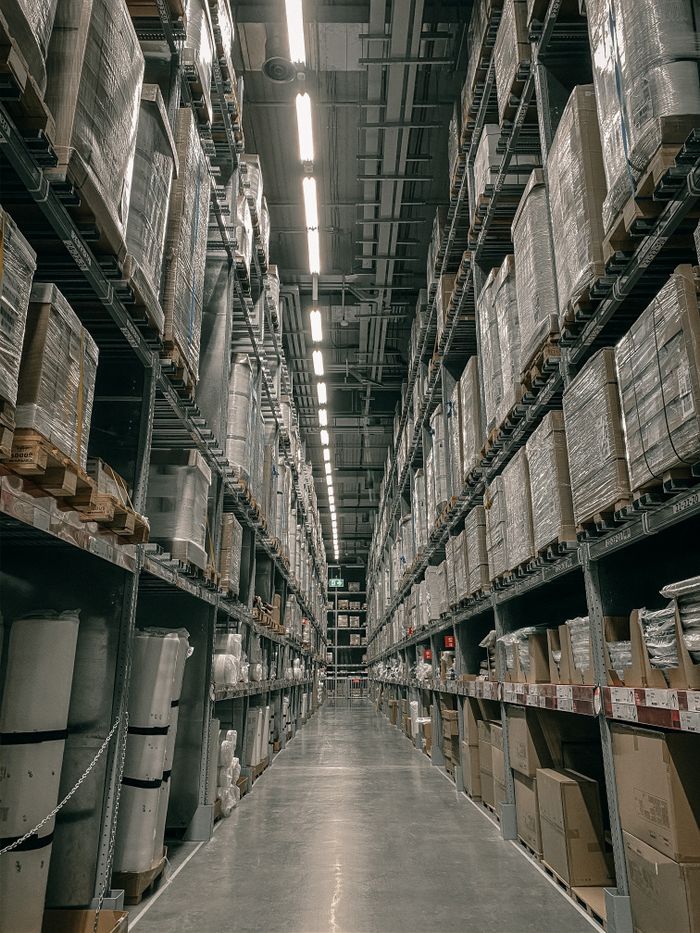 Services A long aisle in a modern warehouse with high shelving filled with boxes and supplies.